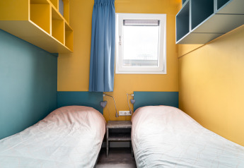To enkeltsenge på et lille værelse med gule vægge og blå accenter i Knilles ved Tusken de Marren, Holland.