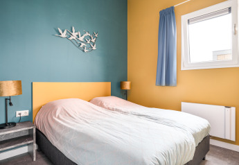 Slaapkamer in de Knilles lodge bij het water in Tusken de Marren, Nederland, met twee aparte bedden en wanddecoratie.