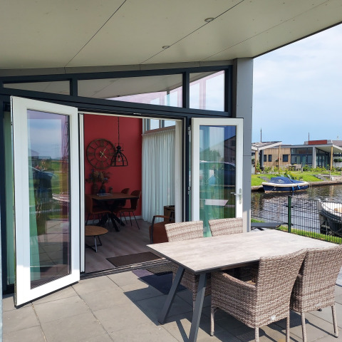 Terraza abierta con mesa y sillas, vista al agua y barcos en el lodge Knilles en Tusken de Marren.