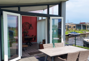Terraza abierta con mesa y sillas, vista al agua y barcos en el lodge Knilles en Tusken de Marren.