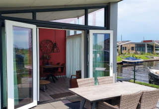Terraza abierta con mesa y sillas, vista al agua y barcos en el lodge Knilles en Tusken de Marren.