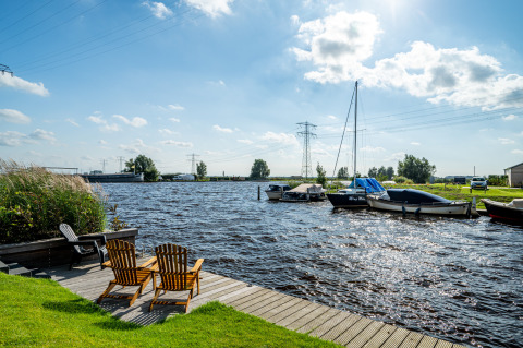 Holzstühle am Knilles-Lodge, Blick aufs Wasser mit Booten bei Tusken de Marren in den Niederlanden