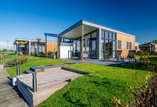 Moderne lodge aan het water bij Tusken de Marren in Nederland, met zonnig terras en gazon.