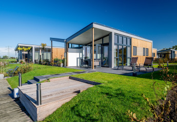 Moderne lodge aan het water bij Tusken de Marren in Nederland, met zonnig terras en gazon.