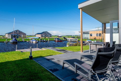 Terrasse mit Liegestühlen am Wasser, Boote und moderne Lodges im Ferienpark Tusken de Marren, Niederlande.