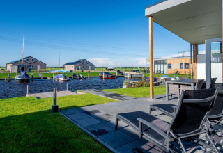 Terrasse med liggestole og udsigt til vand, både og moderne lodges ved Tusken de Marren, Nederlandene.