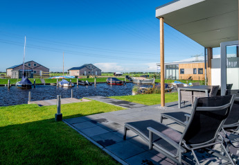 Terrace with sun loungers by the water, moored boats and modern lodges at Tusken de Marren, Netherlands.