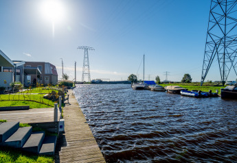Zonnig uitzicht bij lodge Knilles aan het water met boten en moderne woningen in Tusken de Marren.