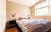 Luminoso dormitorio de glamping con cama doble, cojines coloridos, mesita de noche y gran ventana.