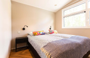 Luminoso dormitorio de glamping con cama doble, cojines coloridos, mesita de noche y gran ventana.
