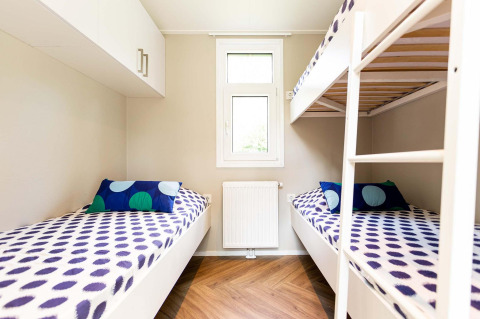 Alojamiento glamping moderno con literas, coloridos cojines, ventana y suelo de madera para familias.