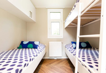 Alojamiento glamping moderno con literas, coloridos cojines, ventana y suelo de madera para familias.