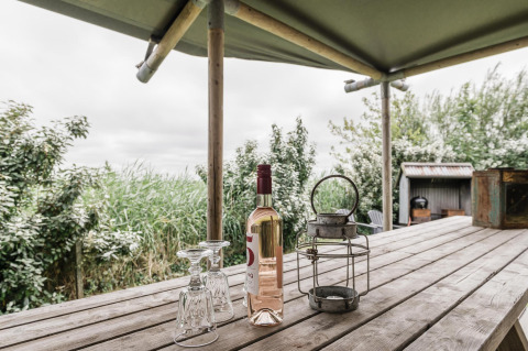 Træbord med vinflaske, to glas og lanterne under overdækket safari telt ved Beach Lodge i Holland.