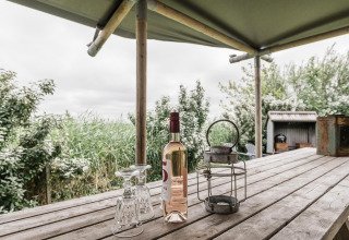 Træbord med vinflaske, to glas og lanterne under overdækket safari telt ved Beach Lodge i Holland.
