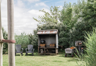 Gartenansicht mit zwei Stühlen, Grillhütte, Fahrrad und Wagen bei Beach Lodge, Duynpark Het Zwanenwater.