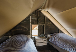 Interior de una tienda safari con dos camas individuales y ropa de cama a cuadros en Beach Lodge, Duynpark Het Zwanenwater.