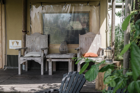 Zona de descanso rústica con sillas de madera ante una tienda safari en Beach Lodge, Duynpark Het Zwanenwater, Países Bajos.