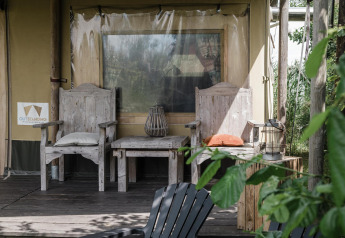Zona de descanso rústica con sillas de madera ante una tienda safari en Beach Lodge, Duynpark Het Zwanenwater, Países Bajos.