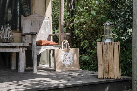 Porche de madera con banco, linterna y bolsa de playa en la tienda Beach Lodge de Duynpark Het Zwanenwater, Países Bajos.
