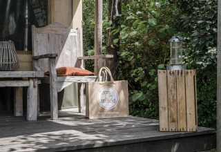 Porche de madera con banco, linterna y bolsa de playa en la tienda Beach Lodge de Duynpark Het Zwanenwater, Países Bajos.