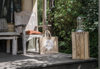 Porche de madera con banco, linterna y bolsa de playa en la tienda Beach Lodge de Duynpark Het Zwanenwater, Países Bajos.