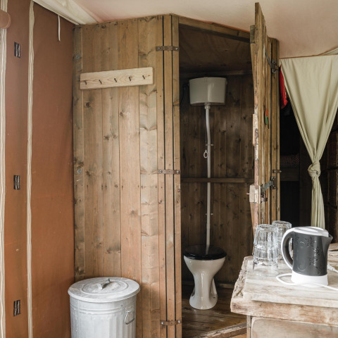Salle de bain rustique en bois dans un lodge, avec toilettes, poubelle, bouilloire et verres.