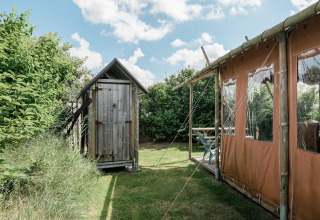 Un cobertizo de madera y una tienda de campaña en Duynlodge, Duynpark Het Zwanenwater, Países Bajos, rodeados de vegetación.