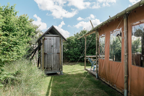Et træskur og et telt ved Duynlodge i Duynpark Het Zwanenwater, Holland, omgivet af grønt under blå himmel.