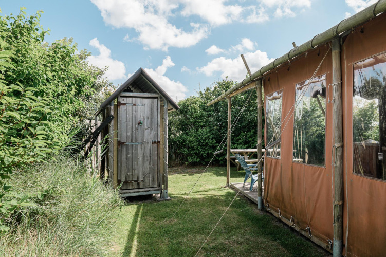 Un cobertizo de madera y una tienda de campaña en Duynlodge, Duynpark Het Zwanenwater, Países Bajos, rodeados de vegetación.