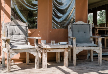 Deux chaises rustiques avec coussins gris et une table sur la terrasse de la Duynlodge à Duynpark Het Zwanenwater.