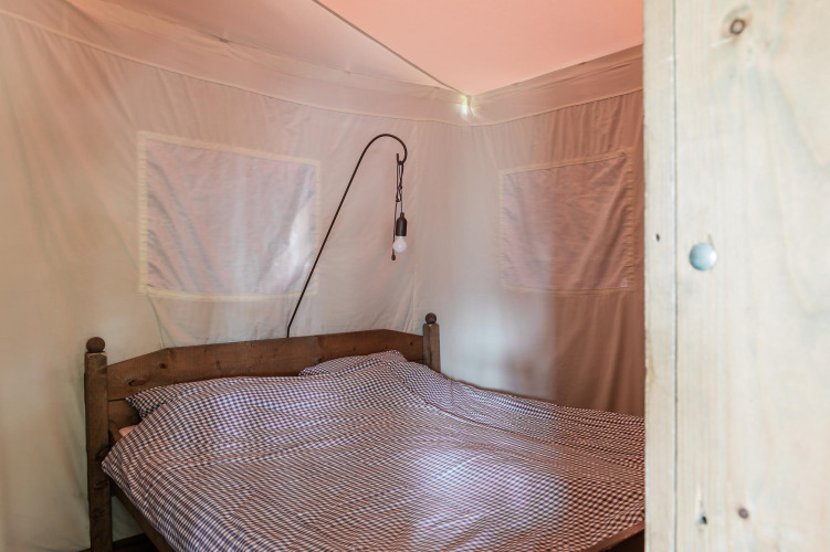 Dormitorio con cama doble y ropa de cama a cuadros en una tienda lodge de Duynpark Het Zwanenwater, Países Bajos.