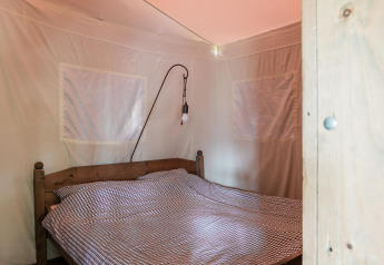 Schlafzimmer mit Doppelbett und karierten Bettbezügen in einer Zeltlodge im Duynpark Het Zwanenwater, Niederlande.