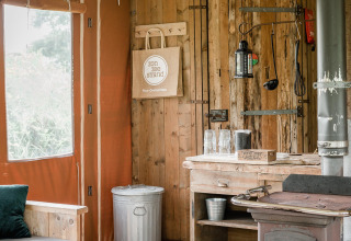 Interior rústico de una cabaña con estufa de leña, mesa de cocina de madera y cubo en Duynlodge, Países Bajos.