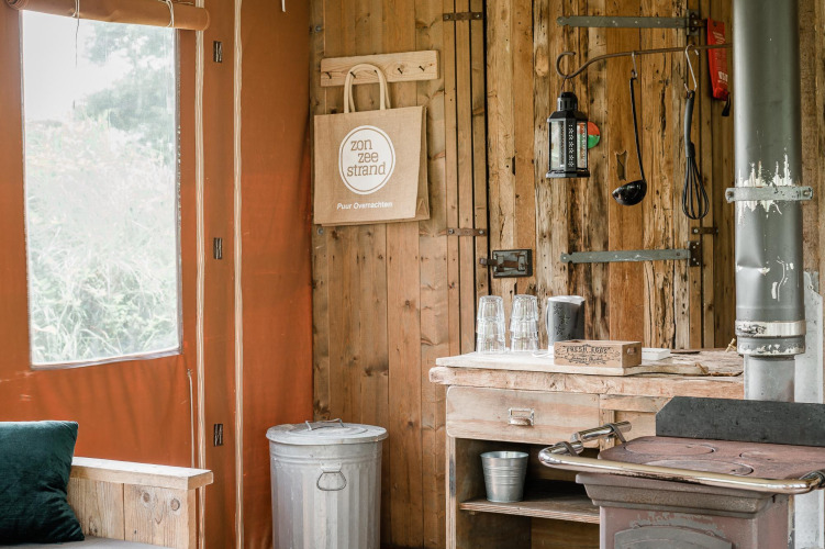 Interior rústico de una cabaña con estufa de leña, mesa de cocina de madera y cubo en Duynlodge, Países Bajos.
