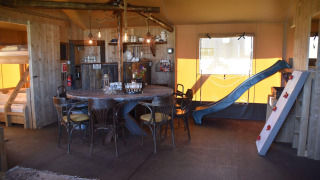 Interno del Kidz Lodge a Duynpark Het Zwanenwater, Paesi Bassi, con scivolo, letti a castello e tavolo.