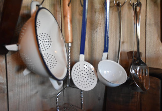 Utensilios de cocina como colador y cucharones colgando en una pared de madera en Kidz Lodge, Duynpark Het Zwanenwater.