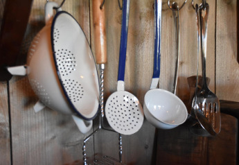 Kitchen utensils including a colander and ladles hanging on a wooden wall at Kidz Lodge, Duynpark Het Zwanenwater.