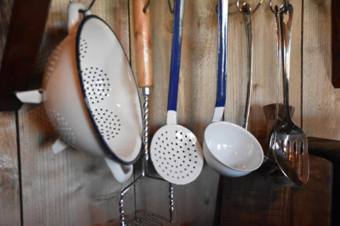 Utensilios de cocina como colador y cucharones colgando en una pared de madera en Kidz Lodge, Duynpark Het Zwanenwater.