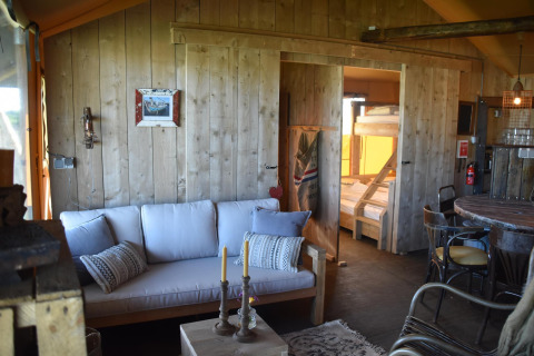 Salon chaleureux en bois du Kidz Lodge à Duynpark Het Zwanenwater, Pays-Bas, avec canapé et lits superposés.
