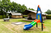 Safari tent at De Tien Heugten in the Netherlands featuring a playground with slide and sandpit on grass.