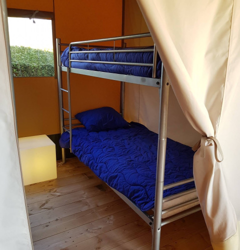 Binnenaanzicht van een safaritent met stapelbedden en blauw beddengoed bij De Tien Heugten in Nederland.