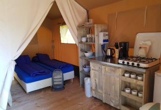 Binnenkant van een safaritent met twee bedden, keukenhoek en houten meubels op De Tien Heugten, Nederland.