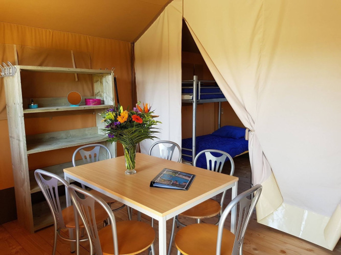 Interior de una tienda safari en De Tien Heugten, Países Bajos, con mesa, sillas y literas visibles.