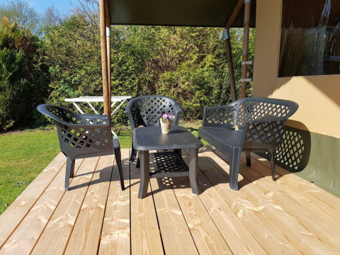 Houten terras met zwarte tuinmeubelen aan een safaritent bij De Tien Heugten in Nederland op een zonnige dag.