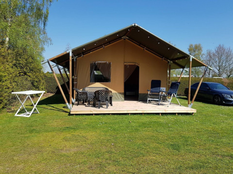 Safari tent at De Tien Heugten in the Netherlands, with a deck, outdoor chairs, table, and car parked nearby.