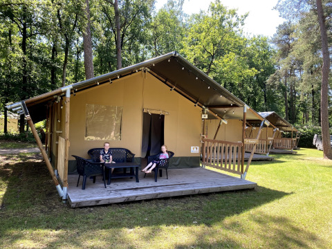 Zwei Kinder sitzen vor einem Safarizelt im Holiday Park Bonte Vlucht in den Niederlanden im Wald.