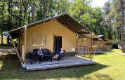 To børn sidder foran en safariteltslejlighed i Holiday Park Bonte Vlucht, Holland, omgivet af træer.