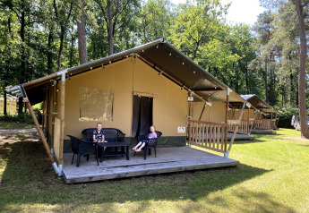 Due bambini seduti fuori da una tenda safari presso Holiday Park Bonte Vlucht nei Paesi Bassi, tra gli alberi.