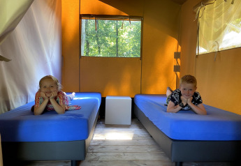 Dos niños tumbados en camas separadas dentro de una tienda safari en Holiday Park Bonte Vlucht, Países Bajos.