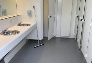 Baño público limpio con lavabos, espejo, herramienta de limpieza y cabinas cerradas en un parque holandés.